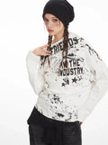 Front view of a woman wearing a white long-sleeve graphic print top with an off-the-shoulder design, styled with dark wash jeans and a black beanie.