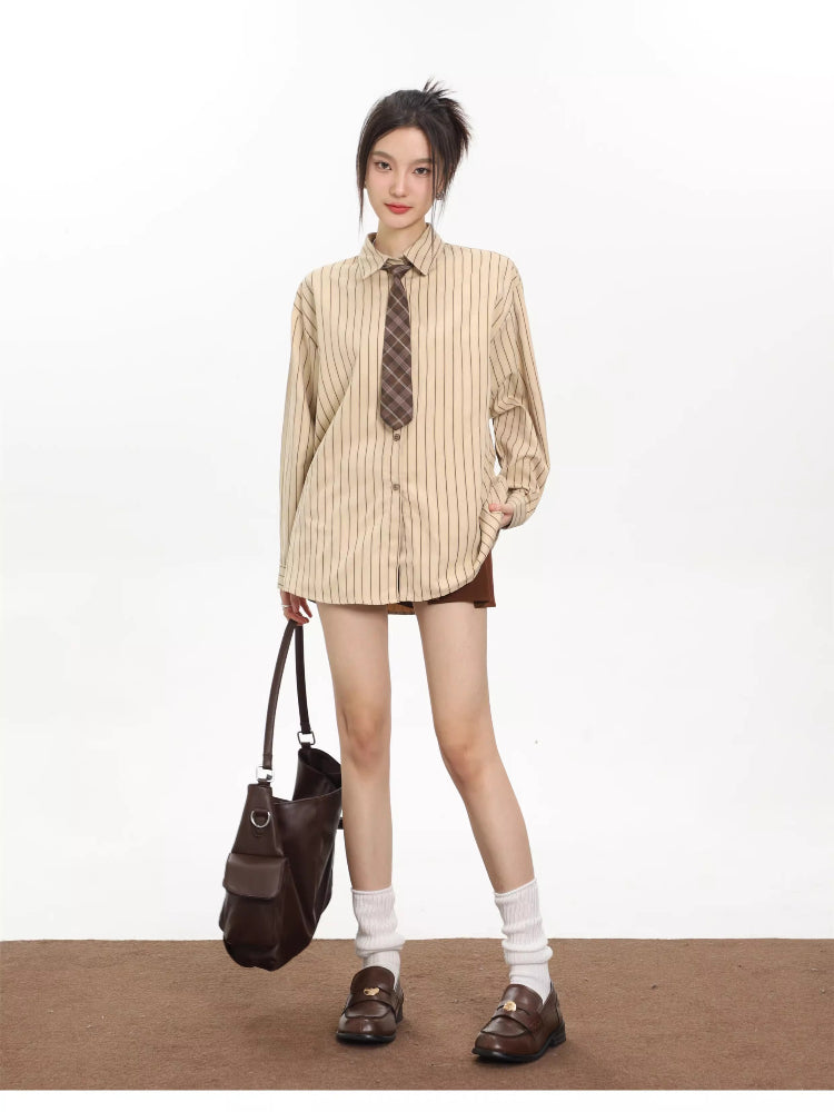 Woman wearing an oversized beige pinstripe button-down shirt with a brown plaid tie, brown skirt, and carrying a brown shoulder bag.