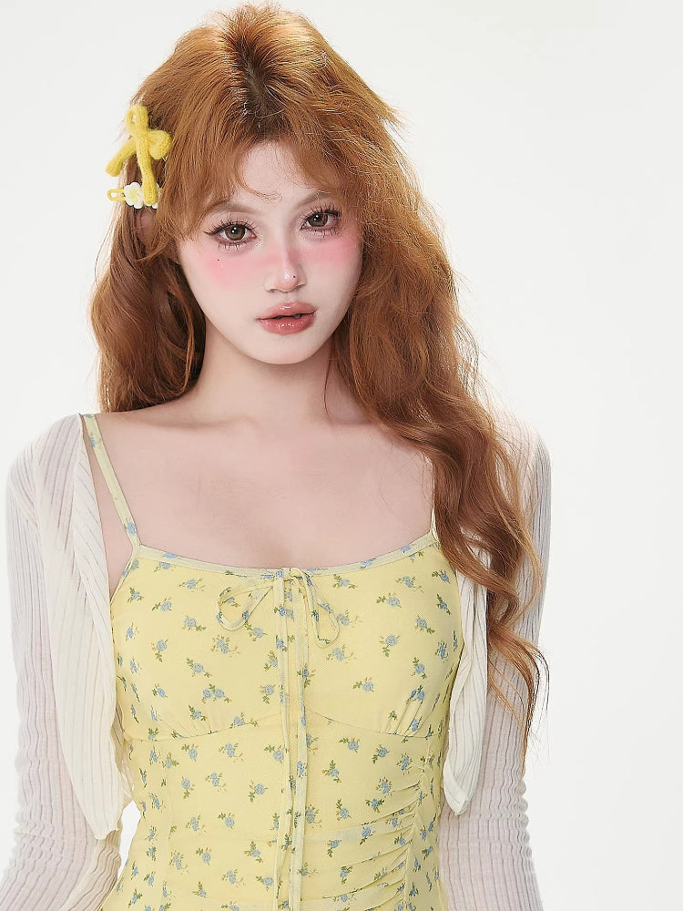 Woman wearing a yellow floral print mini dress with spaghetti straps and a tie front detail, paired with a white sheer long-sleeve shrug.