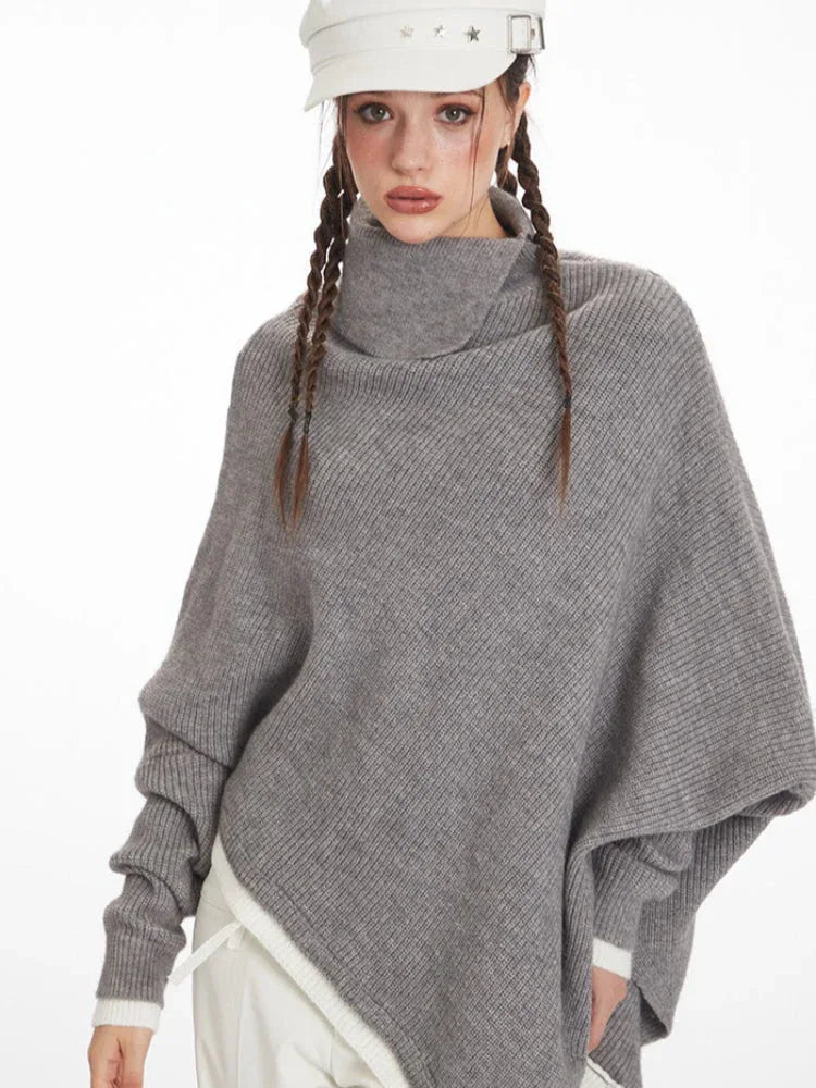 Front view of a woman wearing a grey knit poncho with a turtleneck and batwing sleeves, highlighting the asymmetrical hem.