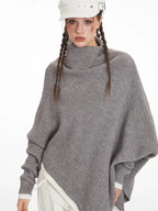 Front view of a woman wearing a grey knit poncho with a turtleneck and batwing sleeves, highlighting the asymmetrical hem.