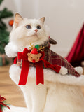 Close-up of a white cat wearing a Christmas cape featuring a reindeer character embellishment and red bows.