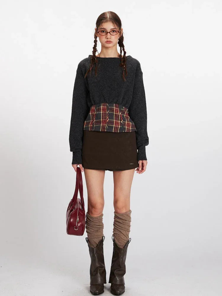 Model wearing a dark grey knit cropped sweater with a plaid waistband accent and a brown mini skirt.
