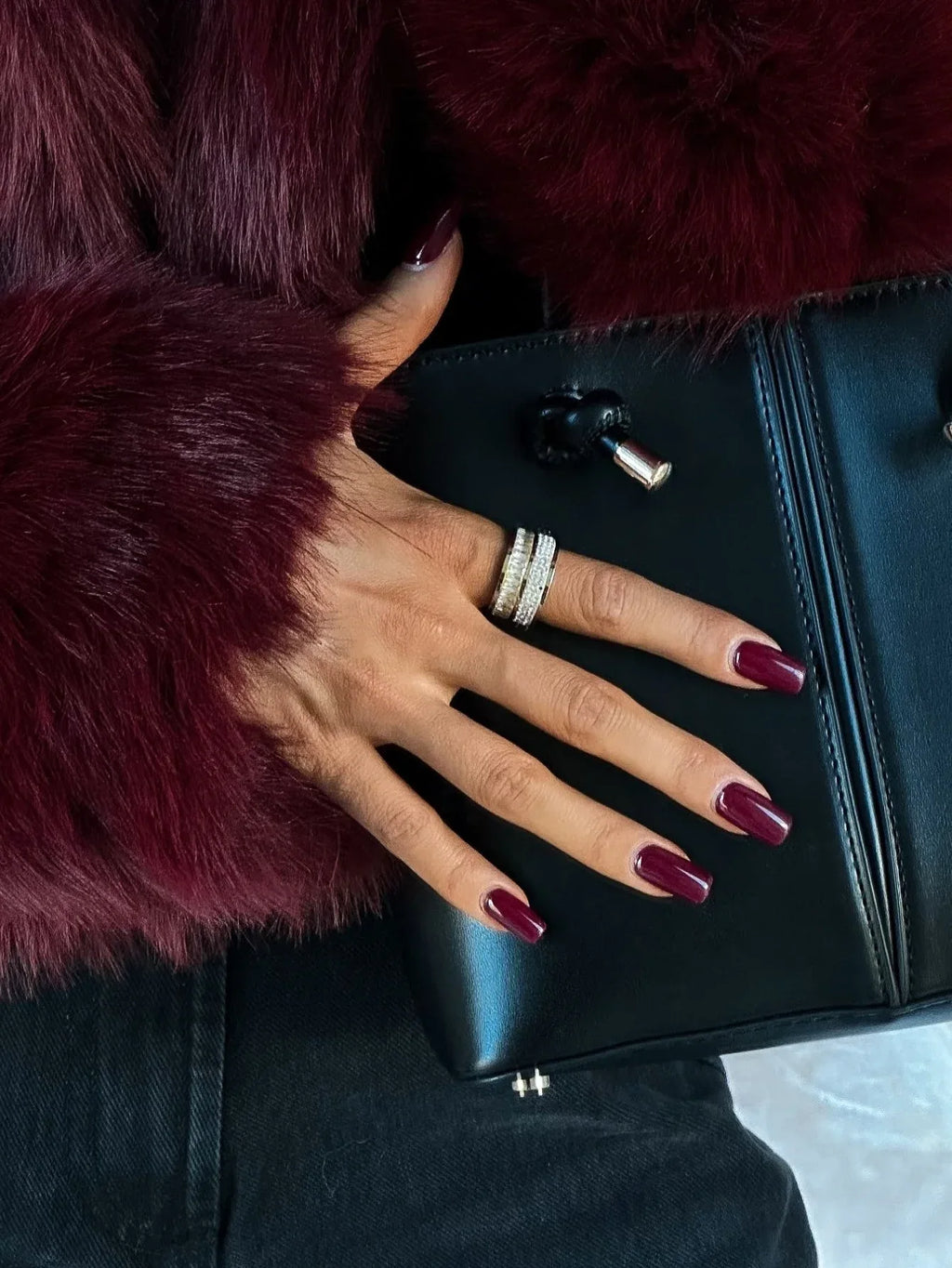 Close-up of a woman's hand wearing rings, showing the texture of a burgundy faux fur jacket.