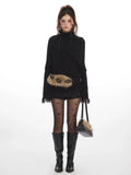 Woman wearing a black turtleneck sweater with fringed cuffs and hem, black shorts, black patterned tights, and black boots