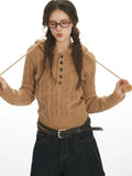 Close-up of a woman wearing a brown hooded cable knit sweater, holding drawstring with pom-pom