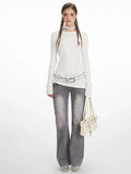 Model wearing a white long sleeve top with asymmetrical seam detail and grey jeans.