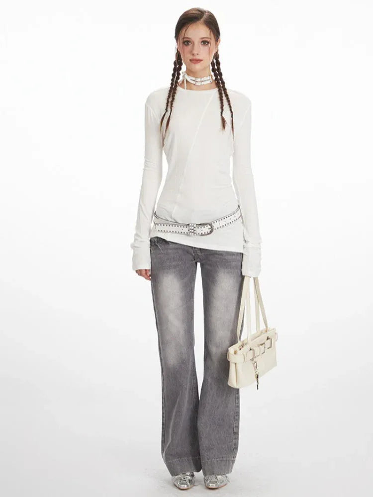 Model wearing a white long sleeve top with asymmetrical seam detail and grey jeans.
