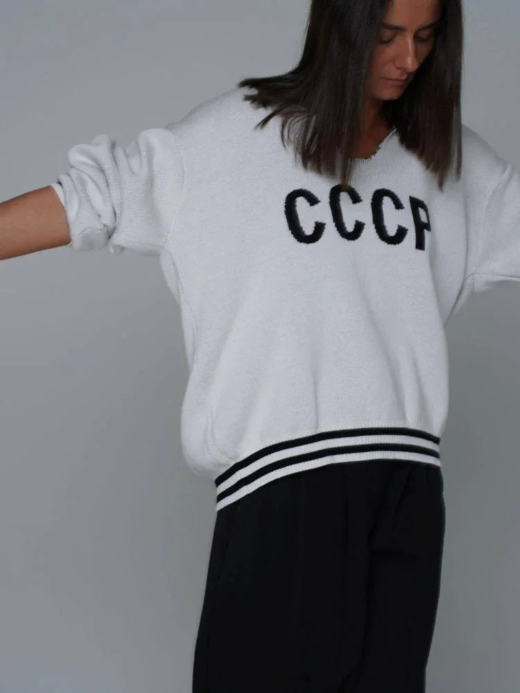 Back view of a woman wearing a white knit sweater with CCCP graphic print and striped collar detail.