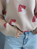 Close-up of a beige knit sweater with a red and white mushroom print, showing ribbed cuffs.