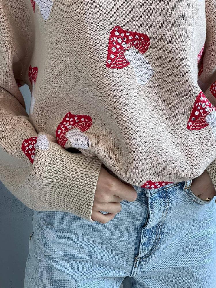 Close-up of a beige knit sweater with a red and white mushroom print, showing ribbed cuffs.