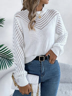 Woman wearing a white long-sleeve knit sweater with openwork details, paired with blue denim jeans and a black belt.