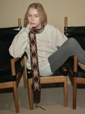 Woman in a sweatshirt and scarf leaning against a wall.