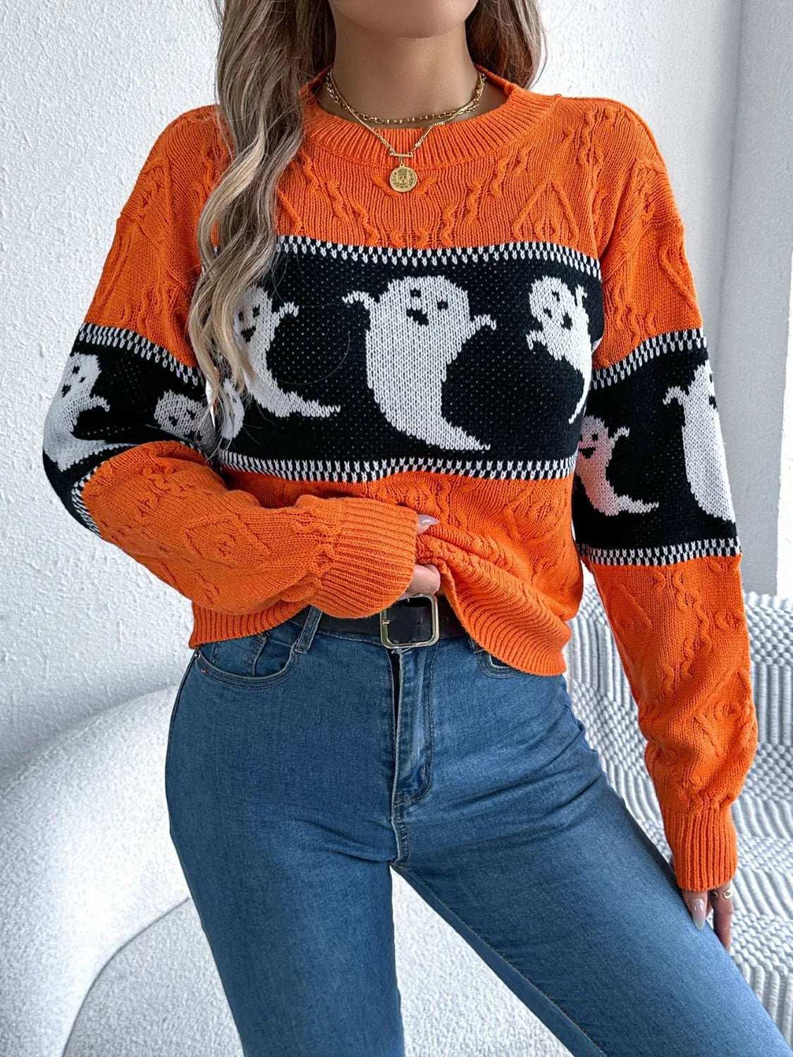 Close-up of a woman adjusting her orange knit sweater featuring a ghost print.