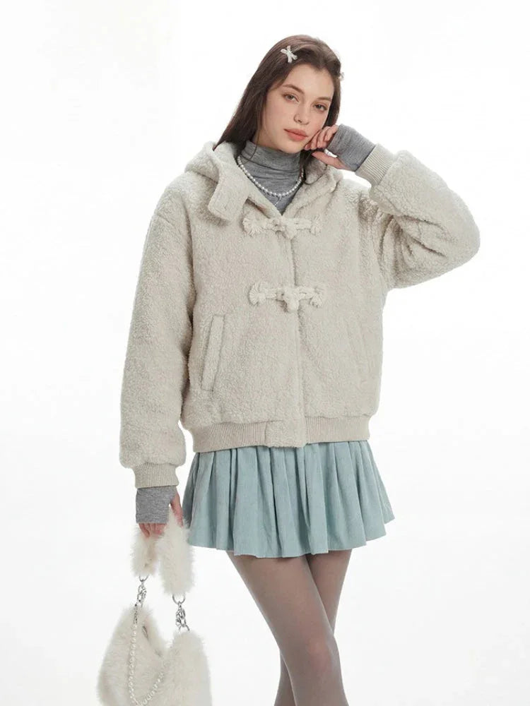 A woman poses in a cream fuzzy hooded jacket, showcasing its toggle closures and relaxed fit.