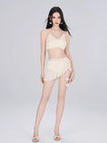 Woman wearing a cream-colored bikini top, wrap mini skirt, and sheer cover-up on a plain background.