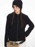 Front view of a woman wearing a black zip-up fleece jacket, white pants, and a black beanie, showcasing the jacket's details.