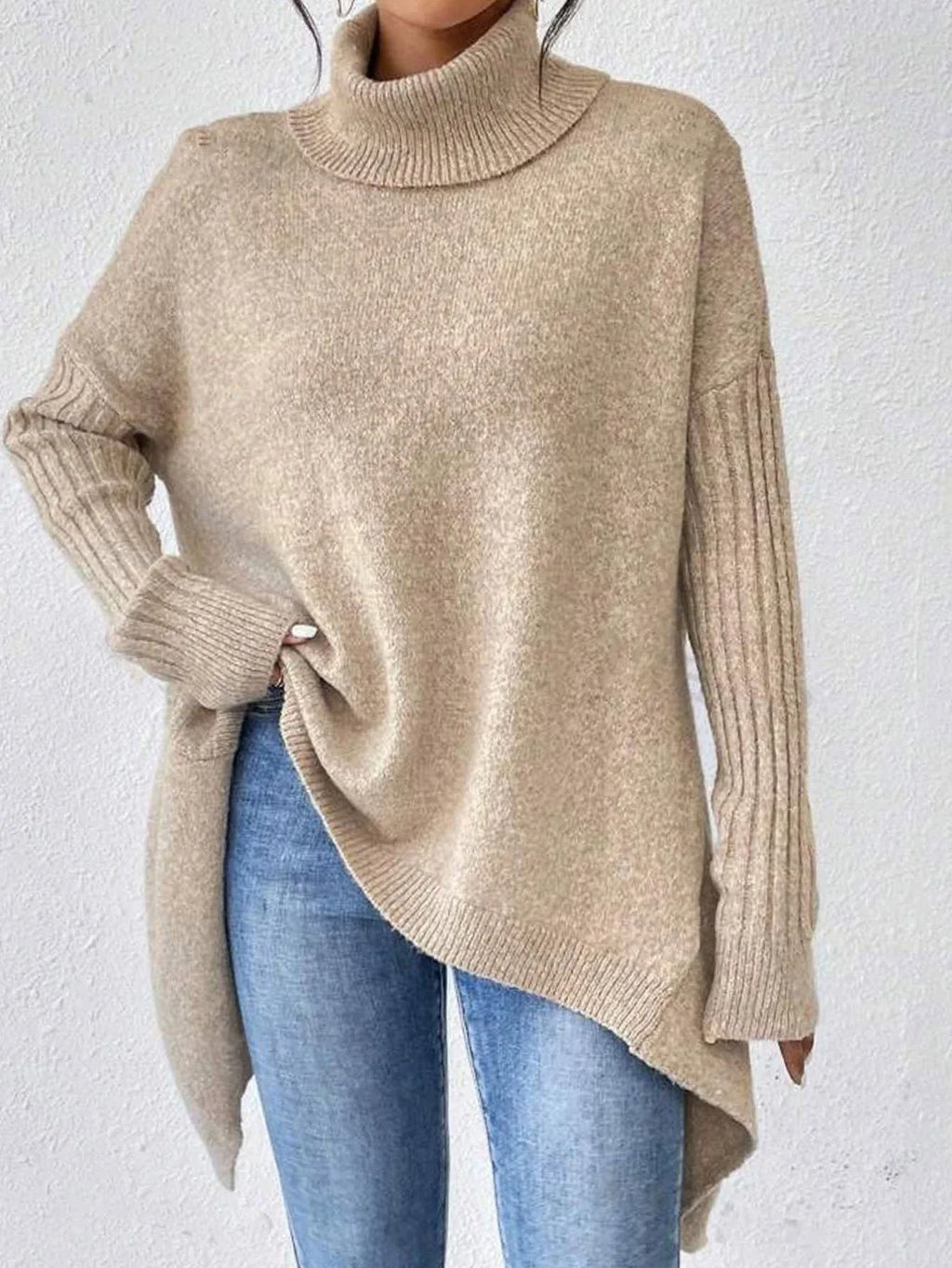 Woman wearing a beige knit turtleneck sweater with ribbed long sleeves and an asymmetrical hem.