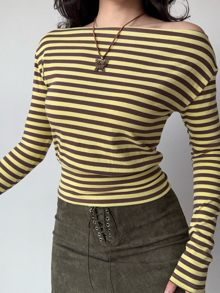 Woman wearing a yellow and brown striped long-sleeve top with an off-the-shoulder neckline and a butterfly pendant necklace.