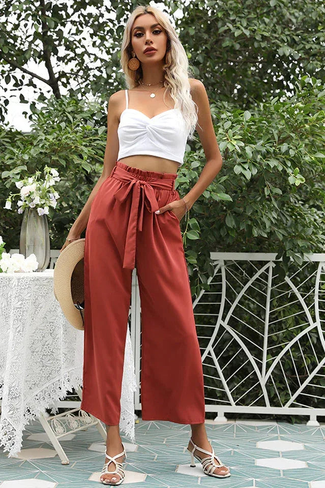 Woman wearing wide leg cropped pants in rust color, paired with a white crop top and sandals Main image