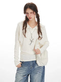 Close-up front view of a woman wearing a white ribbed knit long-sleeve top with a collared button-up neckline and an embellished star pendant necklace.