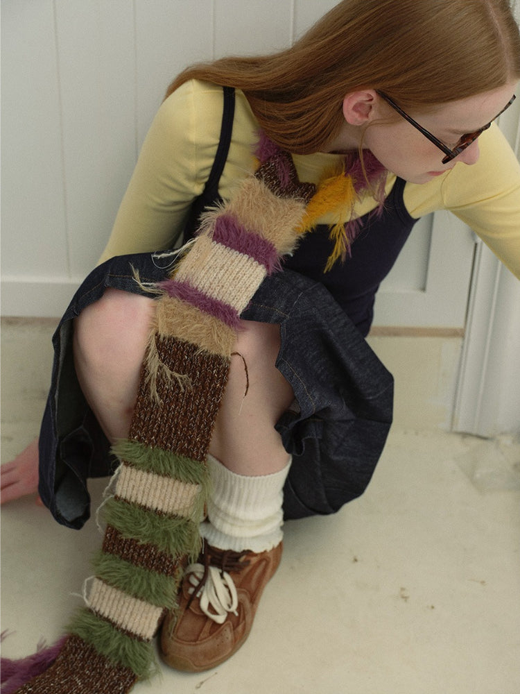 Close-up of a woman's outfit featuring a striped fuzzy scarf draped over her shoulder and chest.