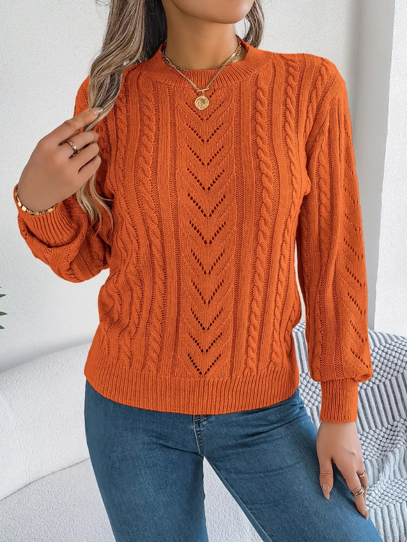 Front view of a woman in an orange knit sweater, showcasing the intricate cable and openwork stitching.