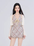 Woman wearing a plaid halter dress with a tie front and ruffled hem, paired with a sheer bolero and yellow earrings.