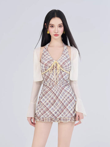Woman wearing a plaid halter dress with a tie front and ruffled hem, paired with a sheer bolero and yellow earrings.