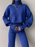 Front view of a woman in a royal blue knit outfit, featuring a turtleneck crop top and high-waisted pants.