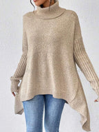 Front view of a woman in a beige knit turtleneck tunic, styled with denim jeans.