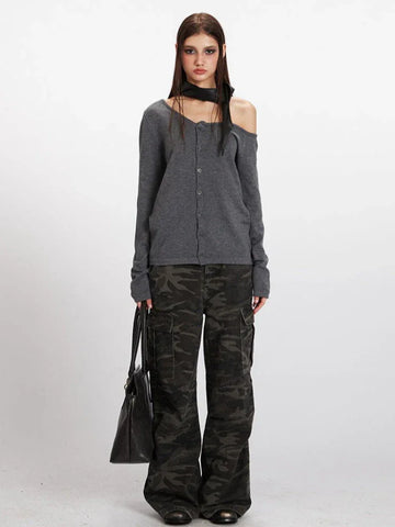 Woman wearing a grey knit cardigan with an asymmetrical neckline and long sleeves, paired with camouflage cargo pants.