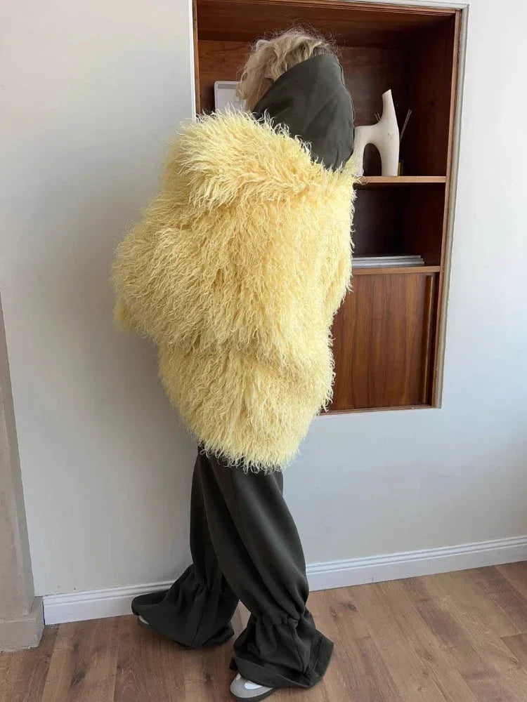 Woman wearing a yellow shaggy faux fur coat from the back, paired with dark green pants and a dark green hood.