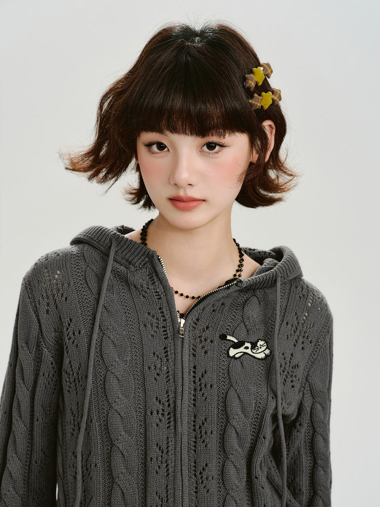 Front view of a model wearing a grey cable knit cropped hooded jacket with ear details and an embroidered patch.
