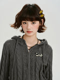 Front view of a model wearing a grey cable knit cropped hooded jacket with ear details and an embroidered patch.