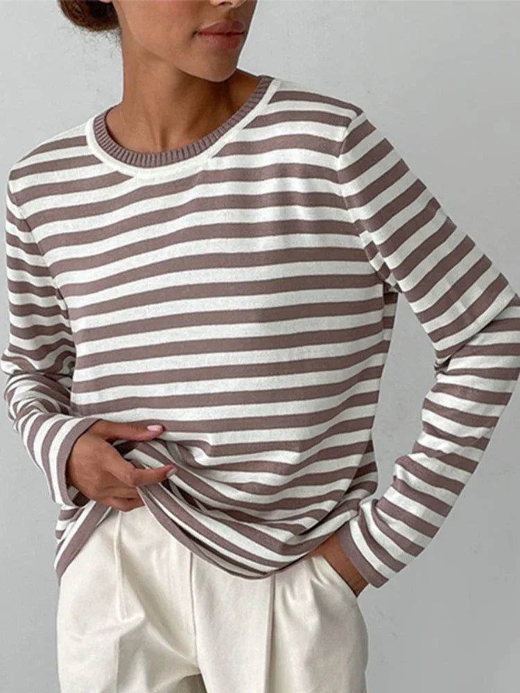 Woman wearing a striped long-sleeve top and cream trousers, hands in pockets.