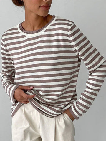 Woman wearing a striped long-sleeve top and cream trousers, hands in pockets.