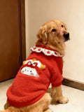 Golden Retriever dog wearing a red fleece dog sweater with a white ruffled collar and embroidered strawberry pattern, sitting and looking to the right