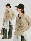 Model posing in a beige knit sweater with a graphic print and distressed cargo pants.