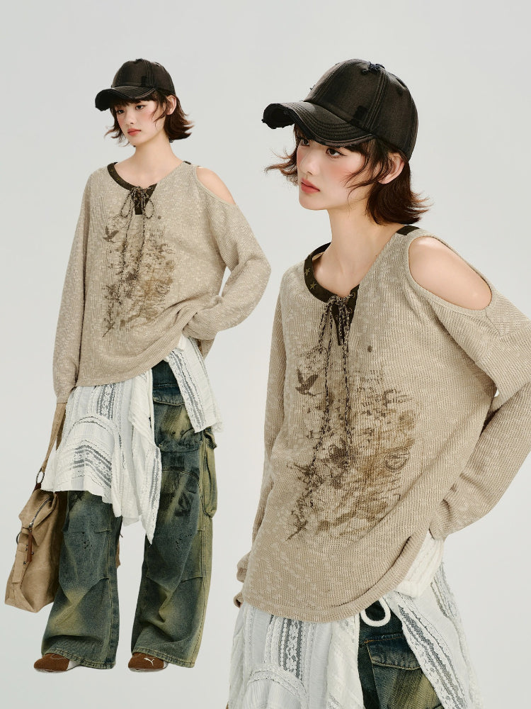 Model posing in a beige knit sweater with a graphic print and distressed cargo pants.