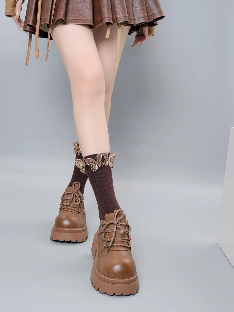 Full view of brown ribbed socks with butterfly details and a ruffled top, worn with brown lace-up platform shoes and a skirt.