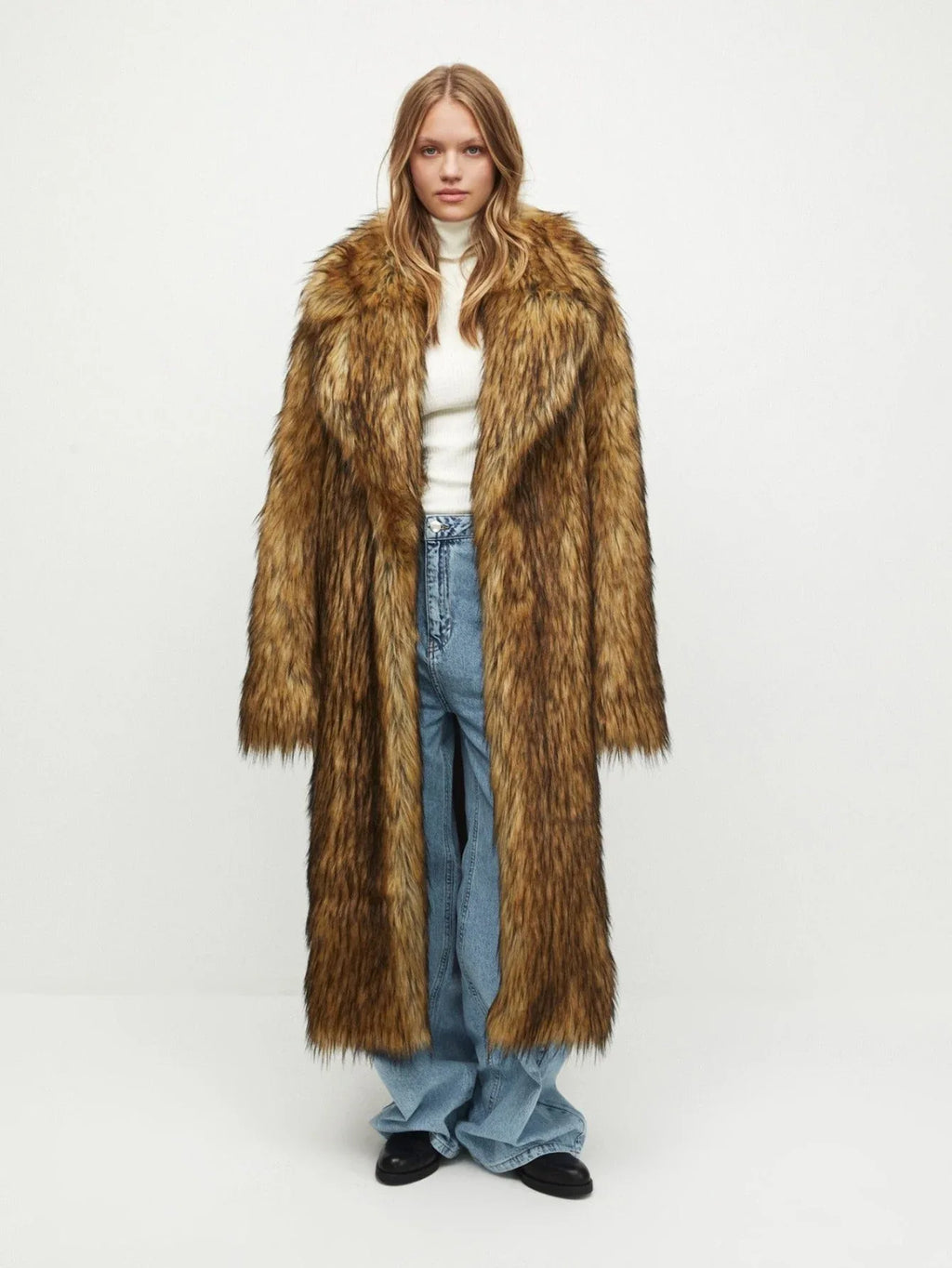 Woman wearing a long brown faux fur coat with a lapel collar and a white turtleneck sweater.