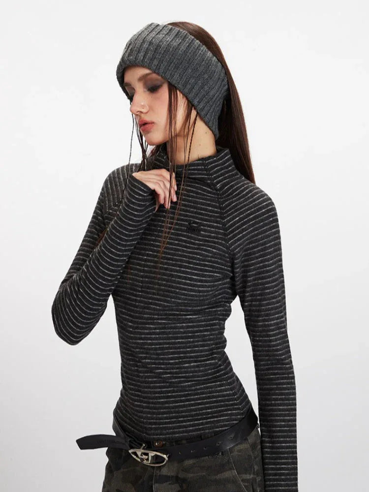 Side profile of a woman wearing a grey striped long-sleeve mock neck top with a quarter zip closure and thumbholes, and a grey knitted headband.