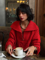Woman wearing a red textured knit half-zip sweater with a spread collar and cable knit detailing, holding a cup of coffee.