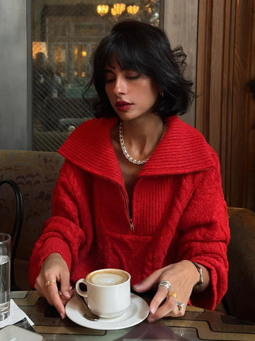 Woman wearing a red textured knit half-zip sweater with a spread collar and cable knit detailing, holding a cup of coffee.