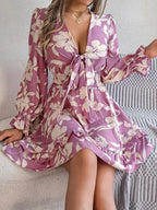 Woman sitting in a mauve purple floral tie-front mini dress