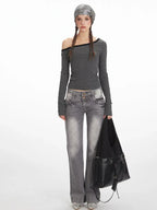 Woman wearing a grey and black striped off-the-shoulder long sleeve top and grey wash jeans, holding a black handbag.