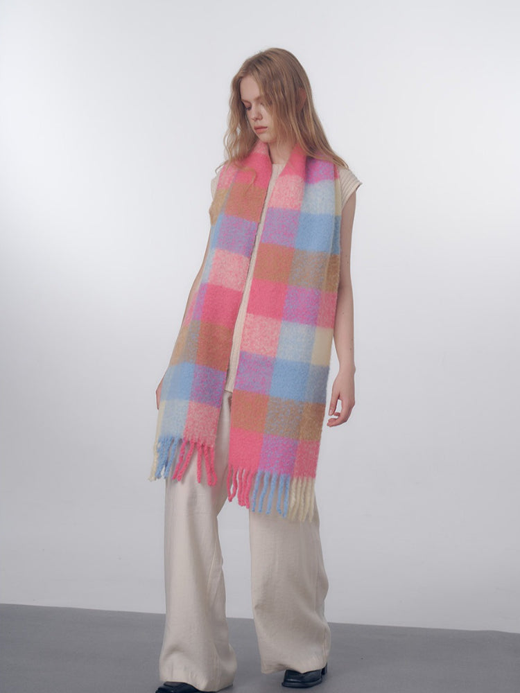 Woman wearing a long, oversized scarf with a pink, blue, and tan plaid pattern and fringed edges.