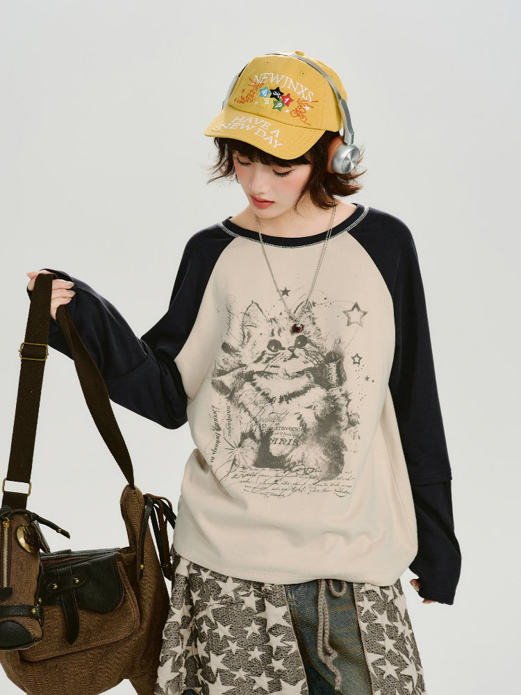 Woman wearing a cream long-sleeve raglan shirt with a graphic cat print and navy sleeves, paired with a patterned skirt and jeans.