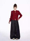 Woman posing with hands on hips, wearing a red cable knit cardigan over a plaid collared shirt and dark wash wide-leg jeans.